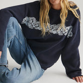 Person wearing a navy blue sweater with lace detailing and light blue jeans